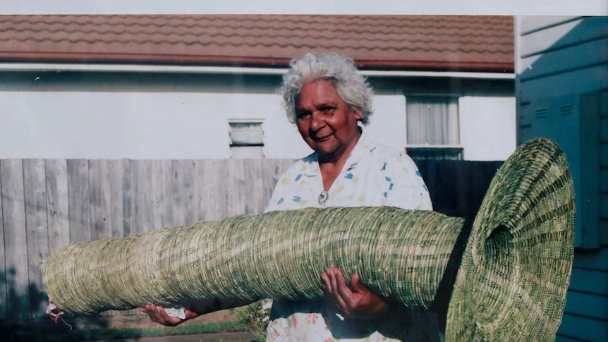 Indigenous basket weaver holding a large trumpet-shaped eel basket