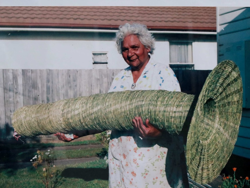 Indigenous basket weaver holding a large trumpet-shaped eel basket