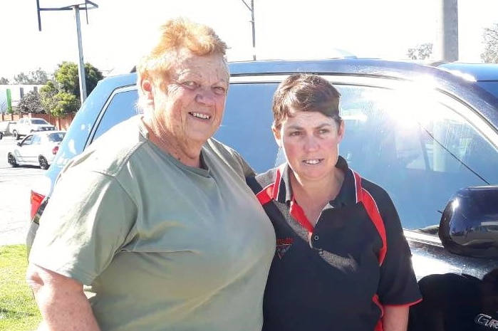 Dot Fox standing with her arm around her daughter Karen in front of her car outside on a sunny day.