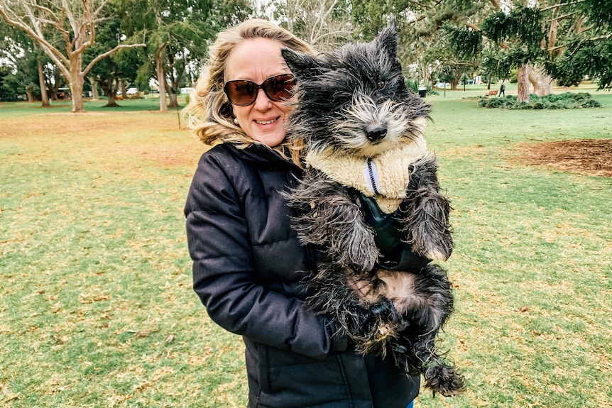 A woman in a big winter coat holds a dog wearing a woollen jumper