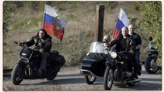 Russian President Vladimir Putin riding a motorcycle among a group of riders showing off Russian flags.
