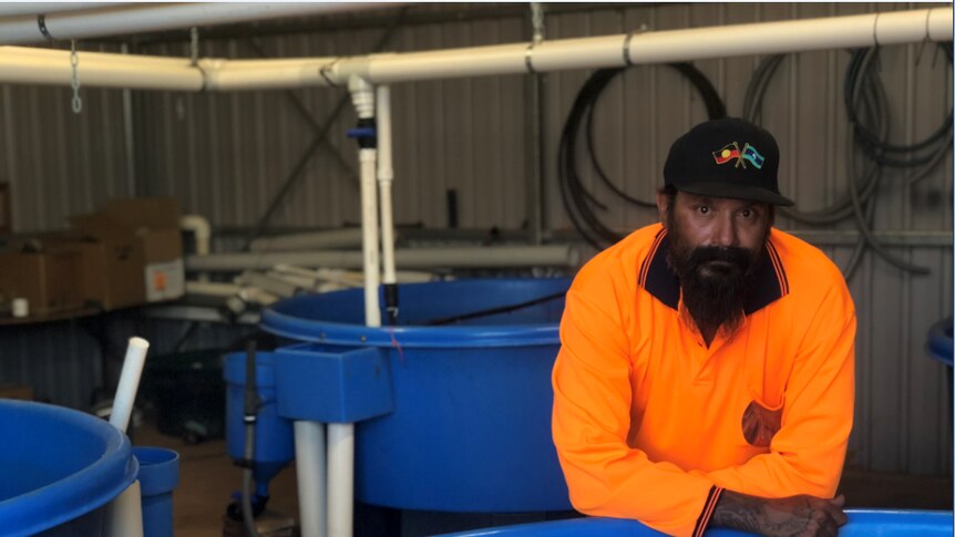Man in orange shirt leaning against blue aquaculture tank