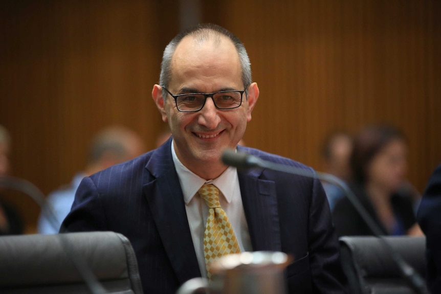 Michael Pezzullo smiles as he looks towards senators out of shot