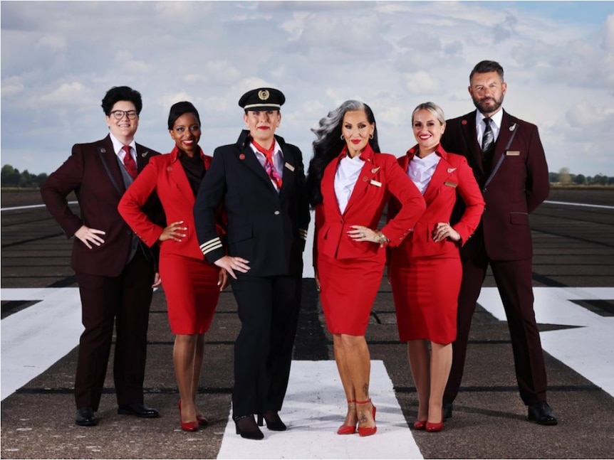Six Virgin Atlantic crew members stand on a runway wearing a range of uniforms from red skirts and jackets to brown suits.