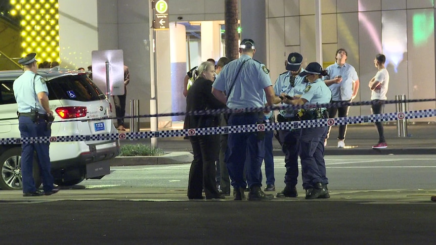 Police stand in a group on a street.