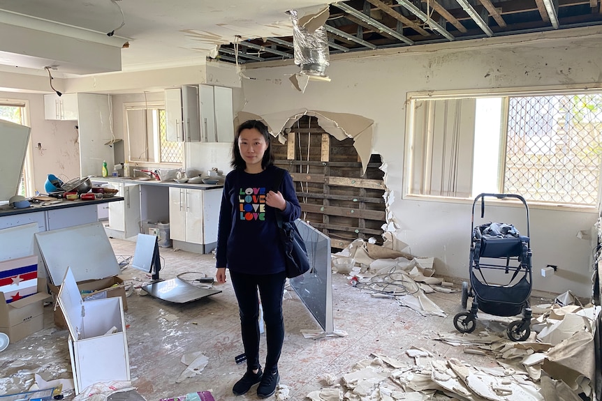 Dark haired woman in dark pants and top stands in derelict house