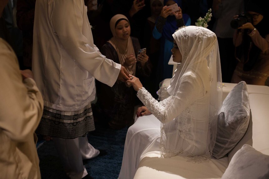 A bride kisses the hand of the groom at a traditional Malay wedding on Christmas Island.