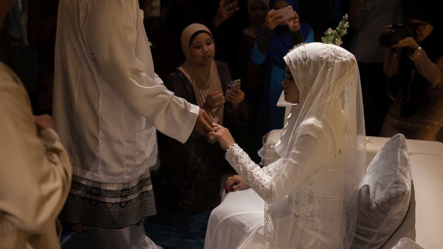 A bride kisses the hand of the groom at a traditional Malay wedding on Christmas Island.