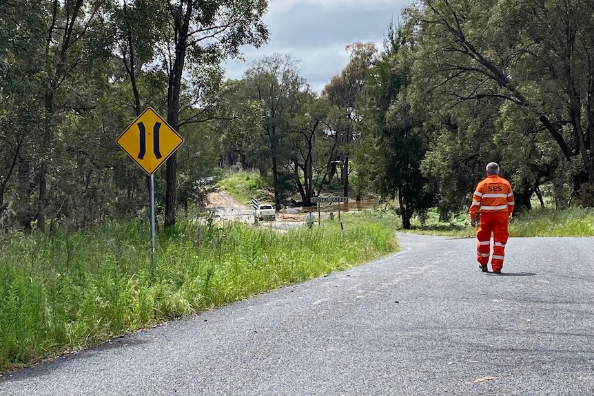 An SES volunteers on a road with a flooded causeway in the distance.