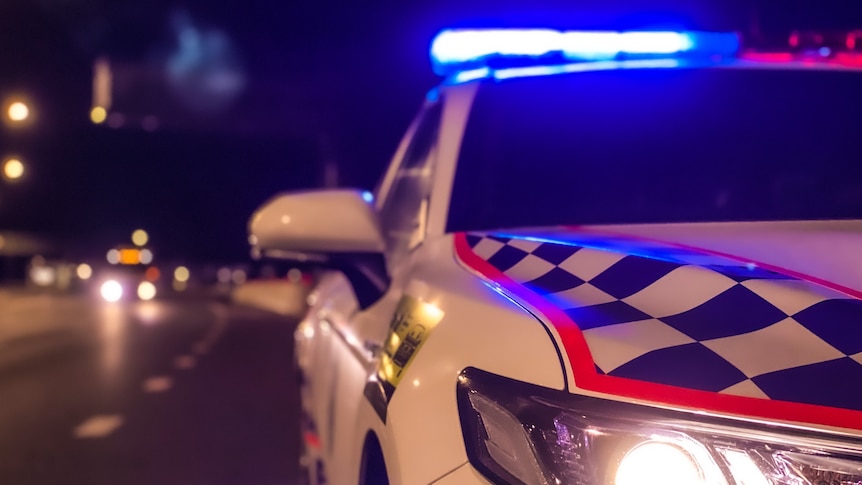 A night time photo of a Queensland Police Service car with its blue light illuminated.