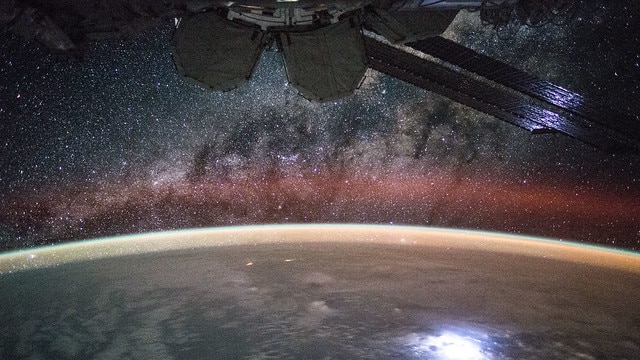 A photo of Earth from outer space with the milky way above it and a space ship in orbit