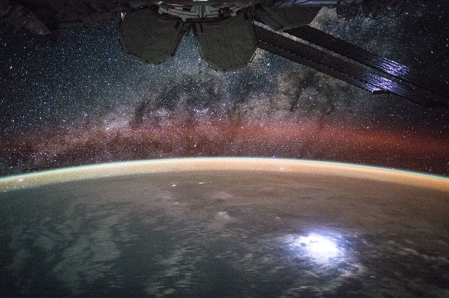 A photo of Earth from outer space with the milky way above it and a space ship in orbit