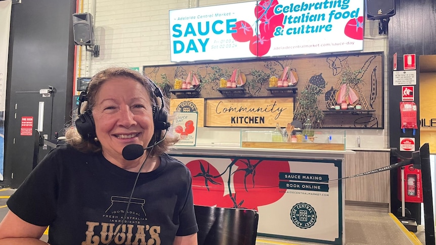 woman in black t-shirt with headphones on leaning on counter of italian restaurant with tomatoes printed on signage in back