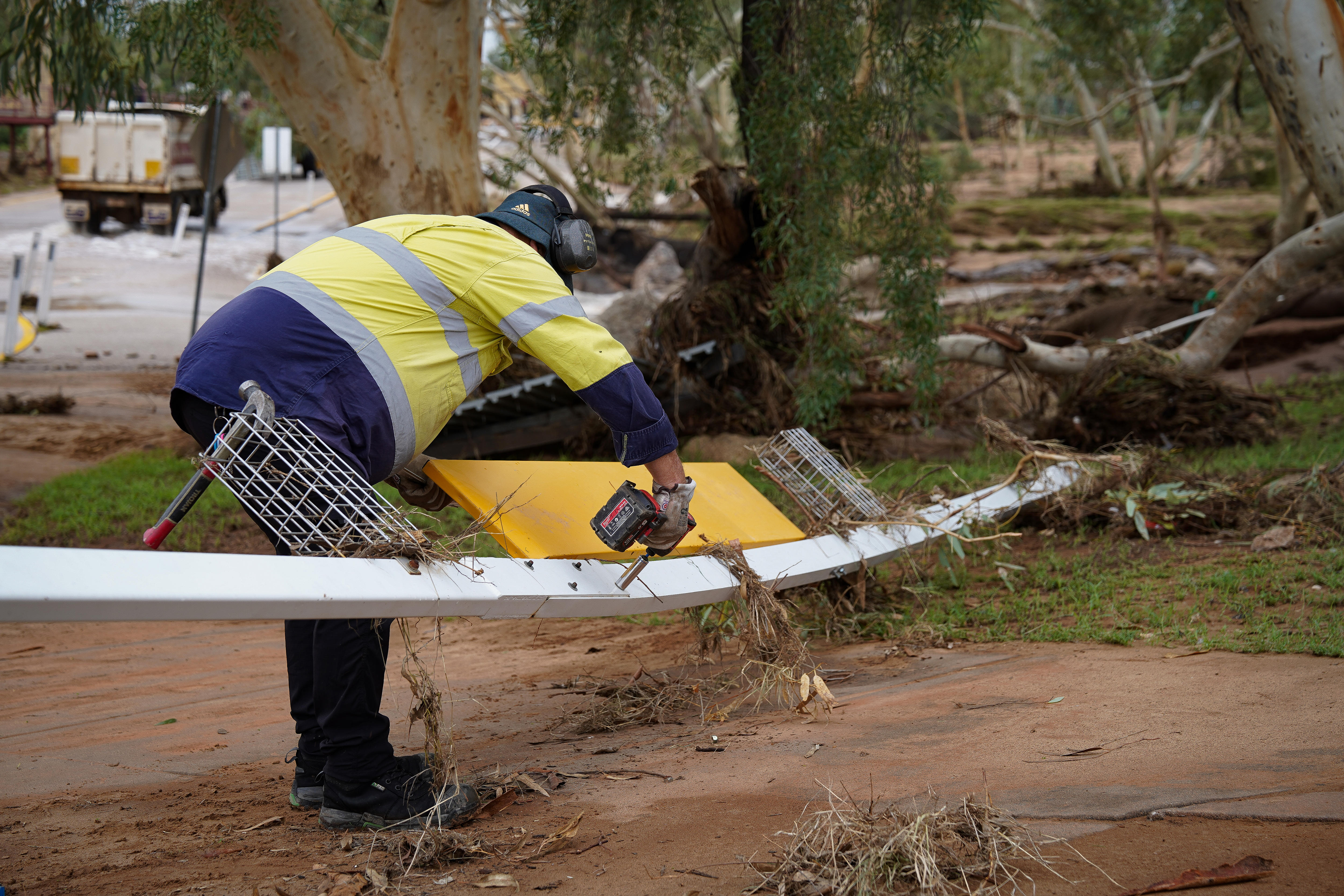 Um homem de short amarelo brilhante se inclina sobre uma grade de metal dobrada para consertá-la