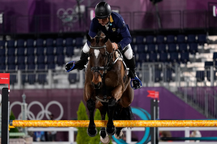 Shane Rose rides a horse as it jumps a yellow pole at the Tokyo Olympics.