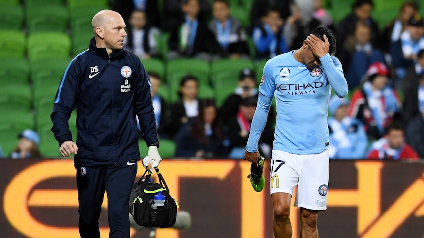 Tim Cahill wipes his face as he leaves the field with shoe in hand accompanied by a medic.