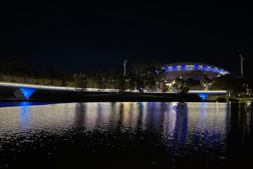 Adelaide Oval and the Torrens footbridge lit up with blue and white lights.