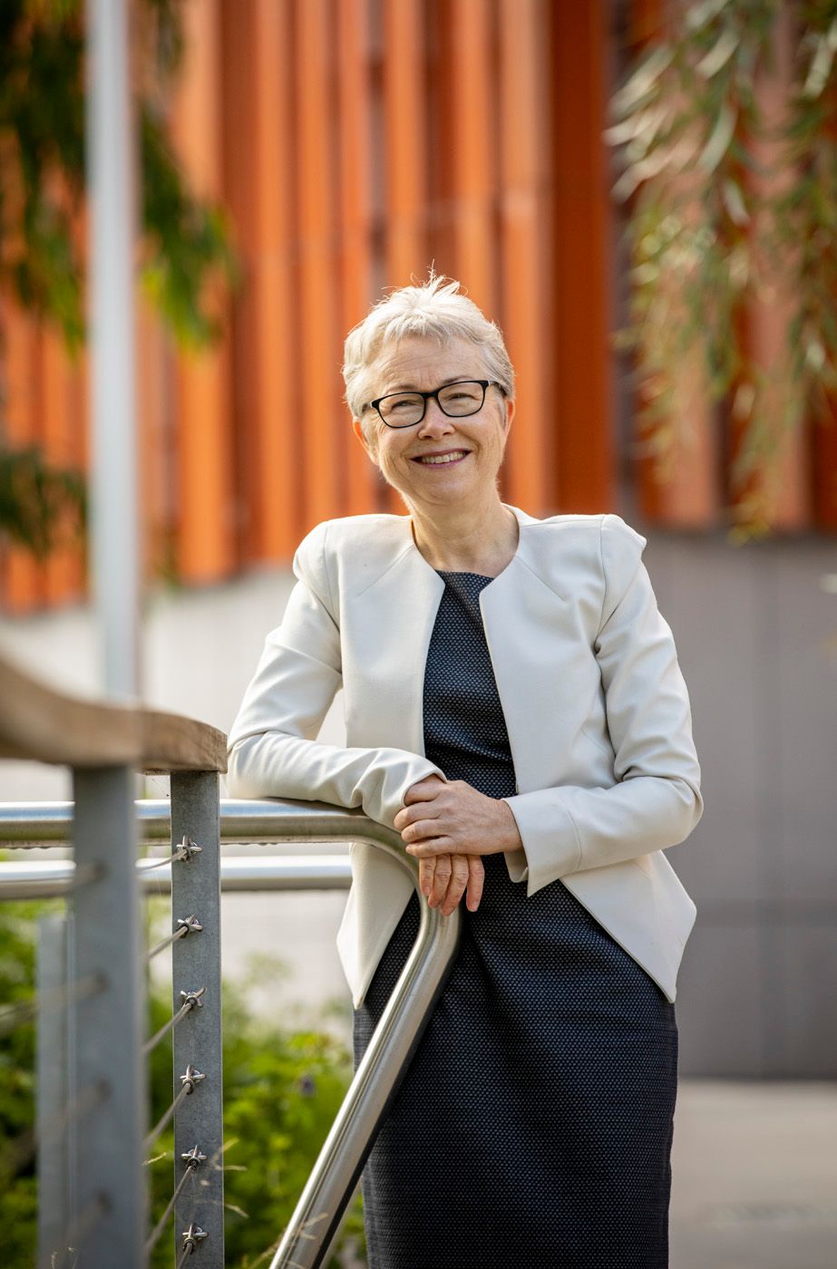A woman with silver-white hair and glasses looks at the camera and smiles