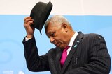 Frank Bainimarama takes off his hat. He is wearing a dapper pinstripe suit with bright magenta tie.