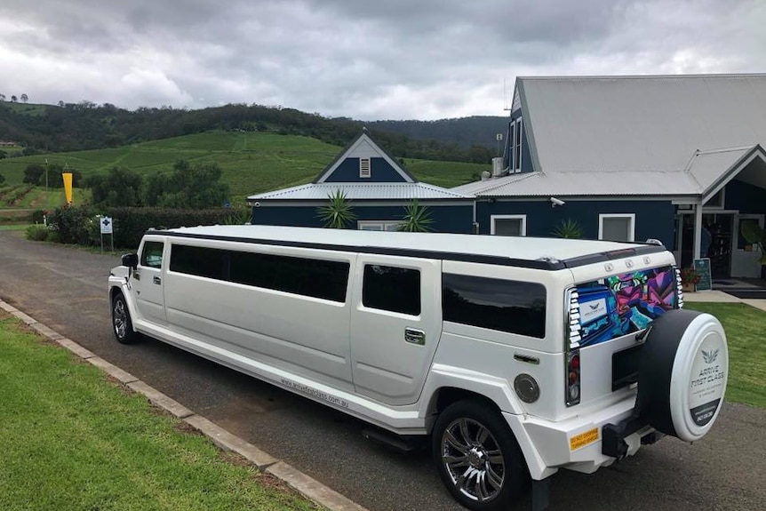 A white stretch Hummer vehicle parked outside a function centre with rolling green hills in the background.