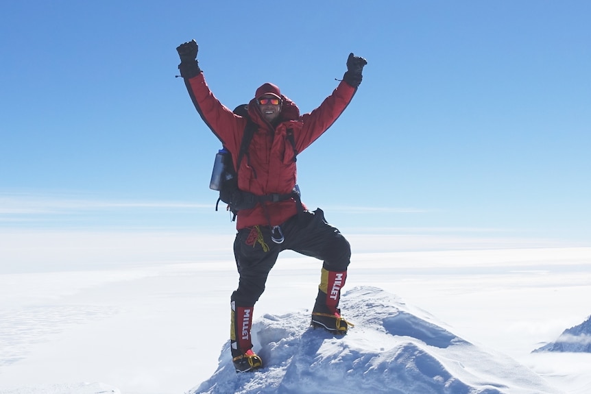 Daniel Bull holding his arms up triumphant on top of a snow-capped mountain.