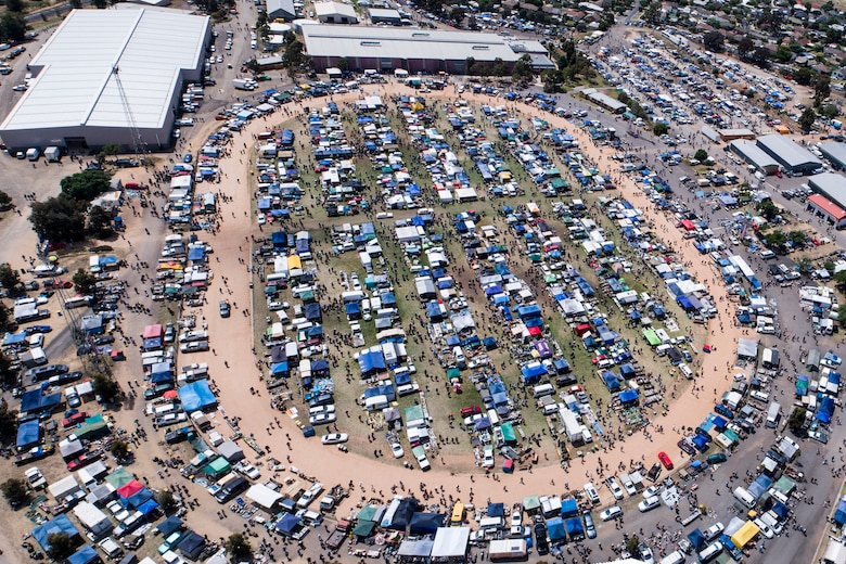An aerial view of hundreds of cars and people scattered around a dusty racecourse.