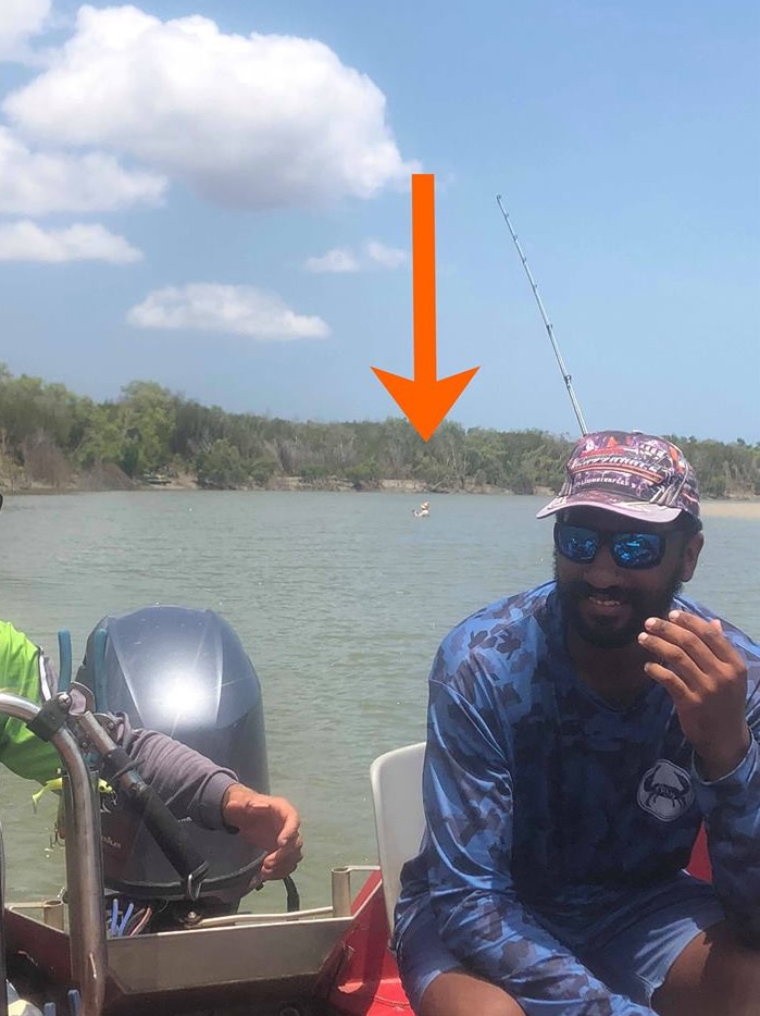 Dan sits in a boat, as a man stands in the water fishing behind him