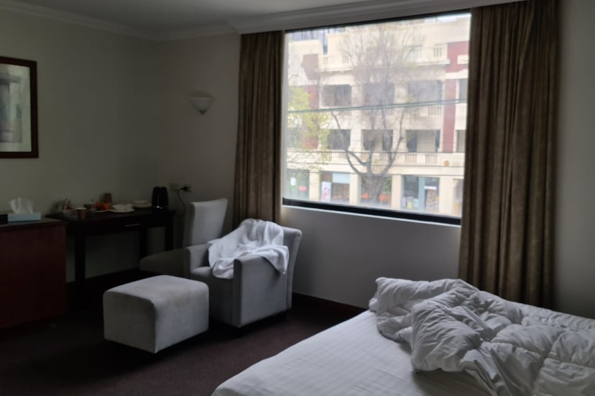 Picture of window and dark hotel room with bed and chairs.