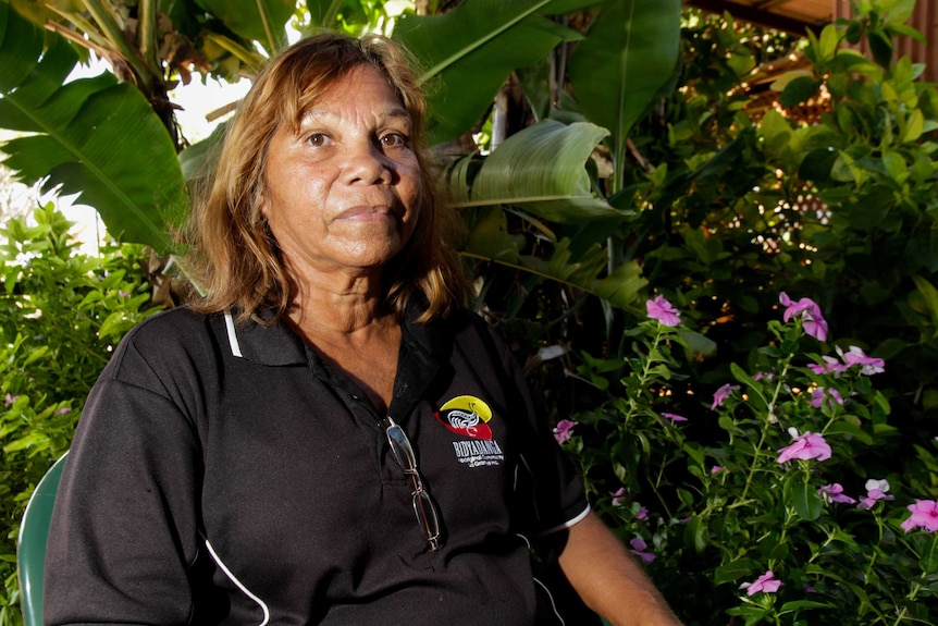 A woman wearing a polo shirt sits in front of a green garden.