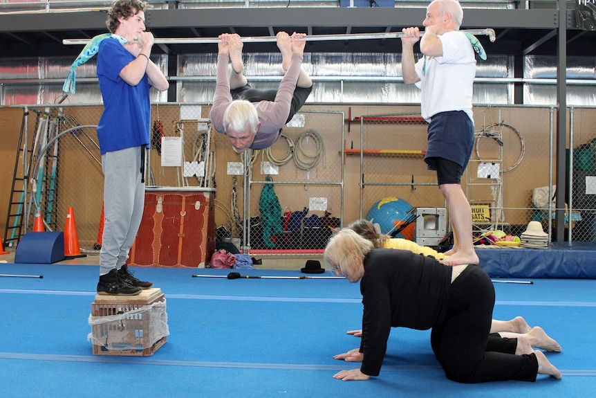 Two people hold a bar on their shoulders while a women performs twists and turns on the bar.