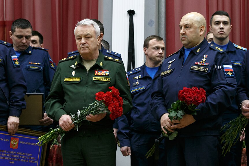 Sergei Surovikin, a bald man in blue uniform, and Nikolai Pankov, in green, clutch bouquets of red roses
