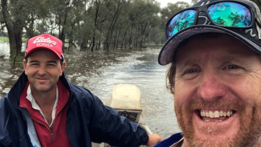 Two men sit in a dinghy riding through floodwaters 
