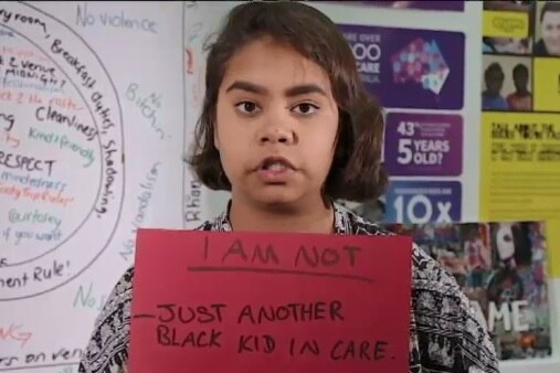 Shanneika holds up a sign saying "I am not just another black kid in state care".