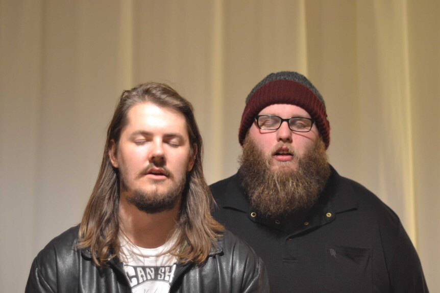 Two men stand with their eyes closed, parodying a typical band photo.