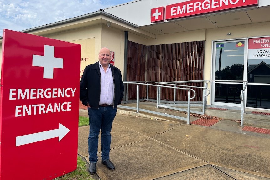 A man stands outside of an emergency entrance at a one story hospital 
