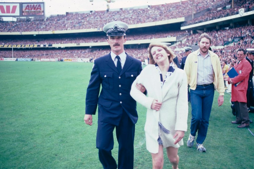 Streaker Helen D'Amico is led off the MCG by a police officer in September 1982 after disrupting the VFL grand final.
