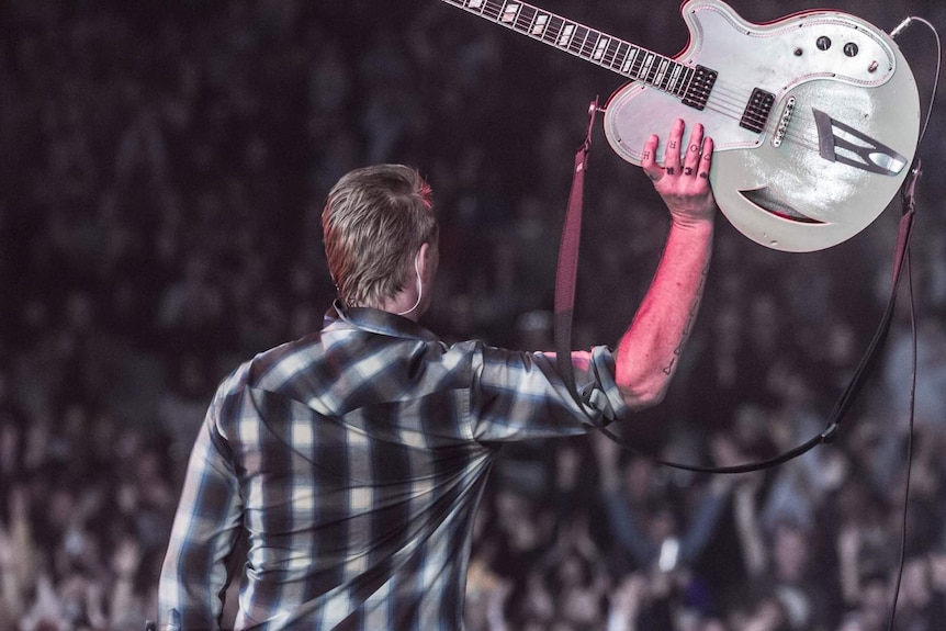 Josh Homme holding aloft his guitar at the end of Queens Of The Stone Age's Splendour 2017 set