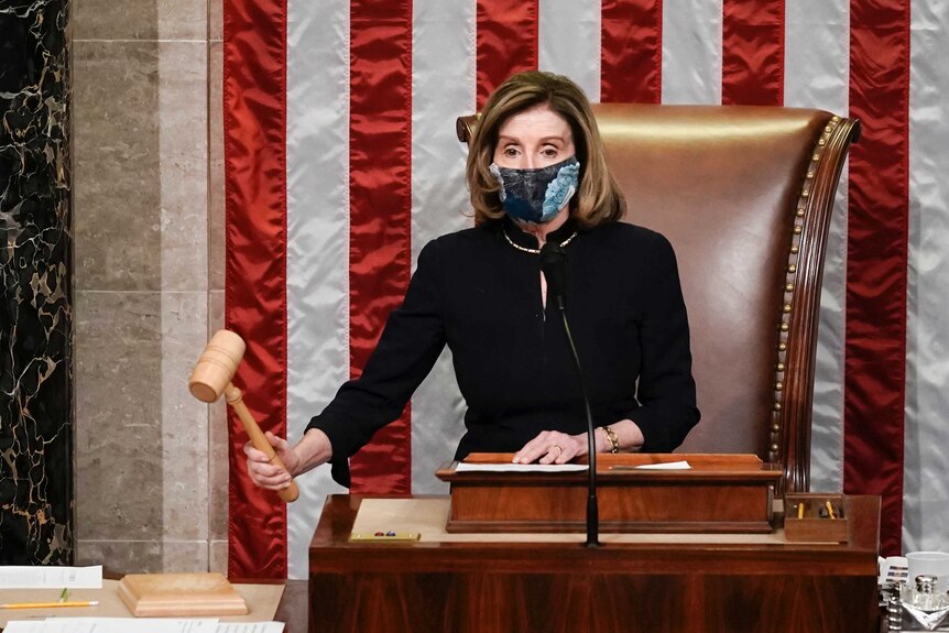 Speaker of the House Nancy Pelosi holds a gavel as she stands before a US flag.