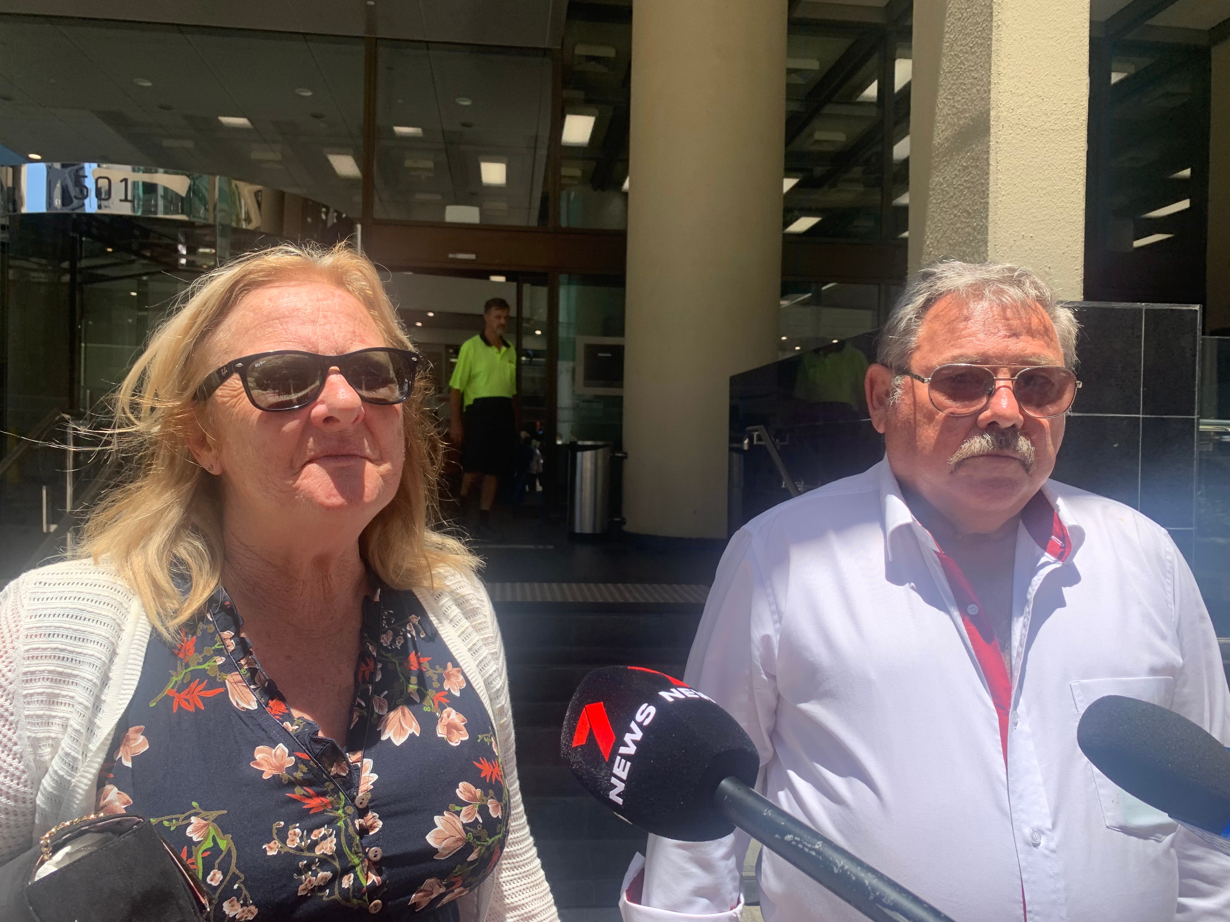 A man and a woman stand outside a court building wearing sunglasses.