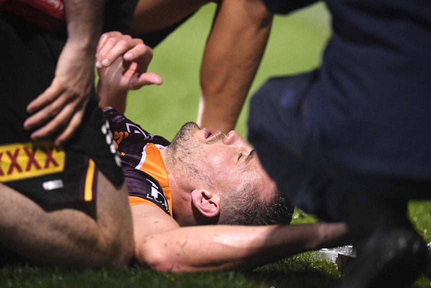 Corey Oates lies on the ground eyes closed as people kneel around him.