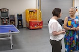 two women standing in a warehouse, with arcade games and a table tennis table