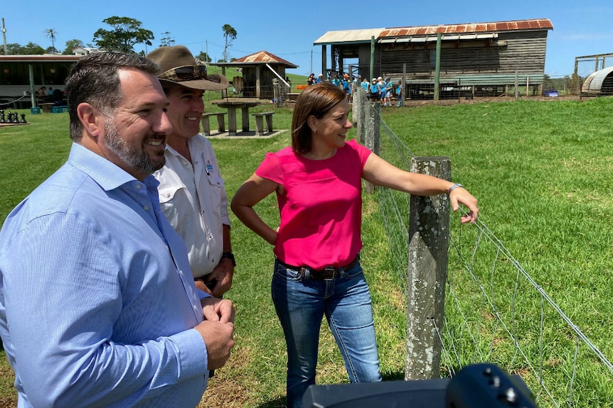 One woman and two men stand at a fence on a dairy farm