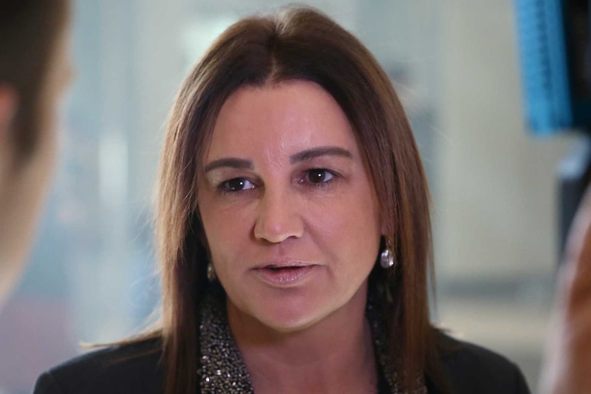 Jacqui Lambie looks to her right as she speaks into a microphone held by a reporter.