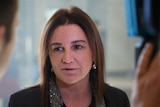 Jacqui Lambie looks to her right as she speaks into a microphone held by a reporter.