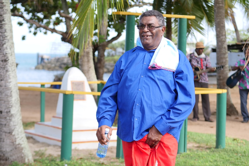 Torres Strait Islander man with blue shirt and towel around his neck is walking.