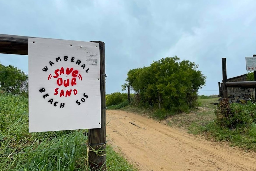 Sign on a wooden fence saying "Wamberal Beach SOS — Save Our Sand"