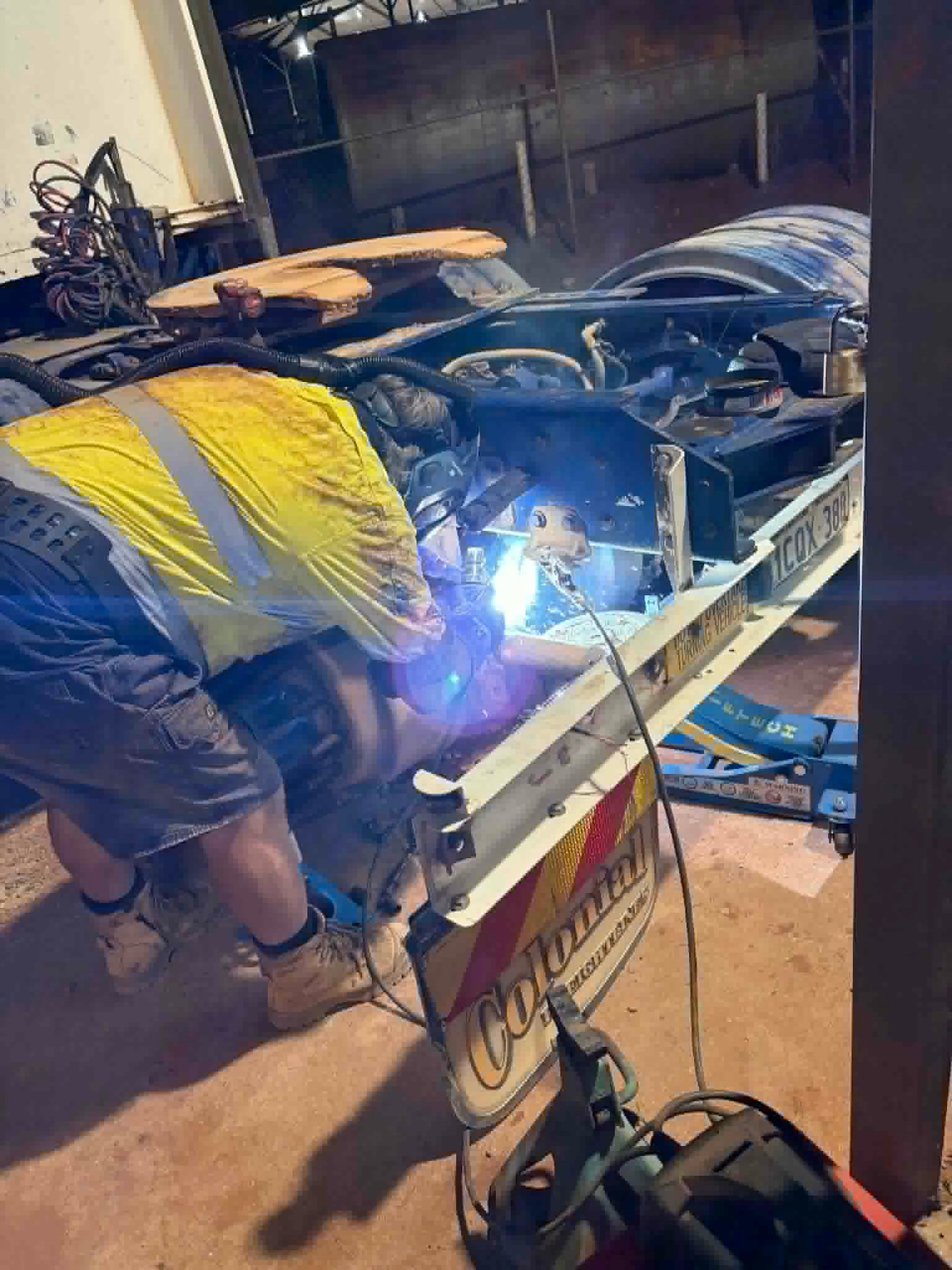 Un hombre de alta visibilidad trabajando con una amoladora angular en la parte inferior de un camión