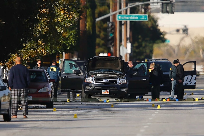 FBI and police continue their investigation around the area of the SUV vehicle where two suspects were shot by police following a mass shooting in San Bernardino