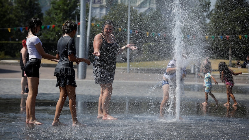 Adults and children play in a water fountain during hot weather in the UK.