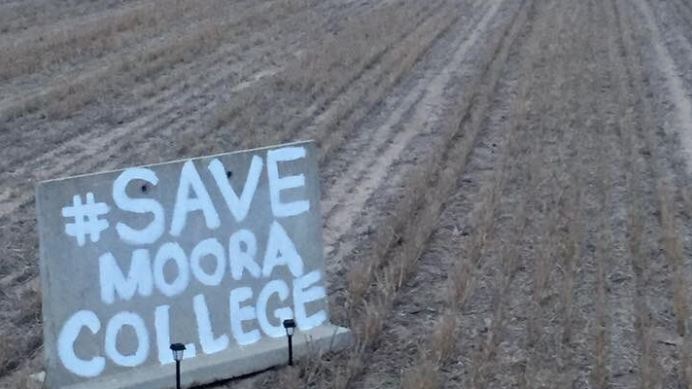 Wooden sign with words painted in white: #Save Moora College in a plowed field